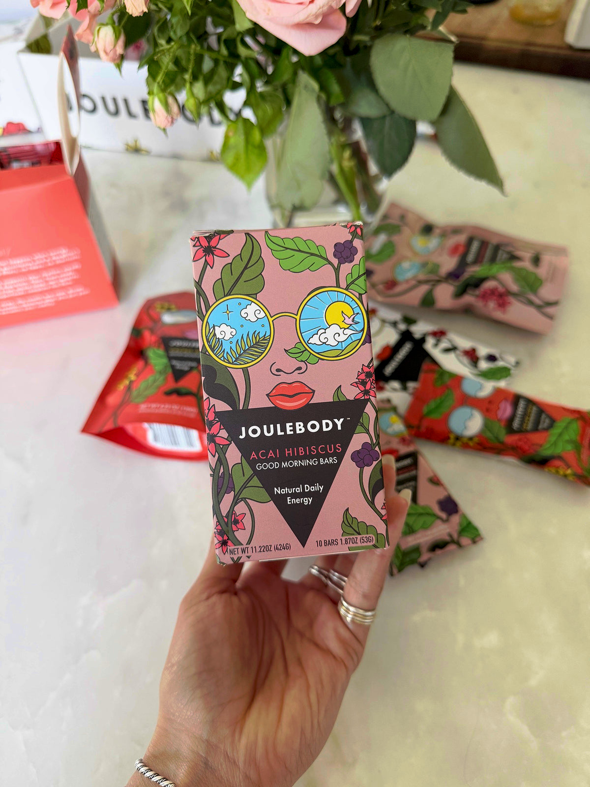 Holding a box of Açaí Hibiscus Good Morning bars